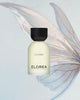 A frosted glass bottle of ELOREA CLOSER fragrance with a matte black cap, centered against a pale blue background with a large translucent wing graphic behind it.